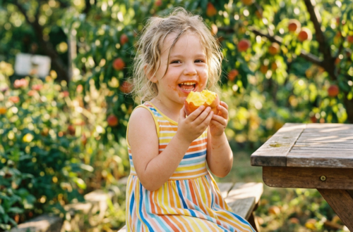 Smiling child in striped dress eating an apple in an orchard